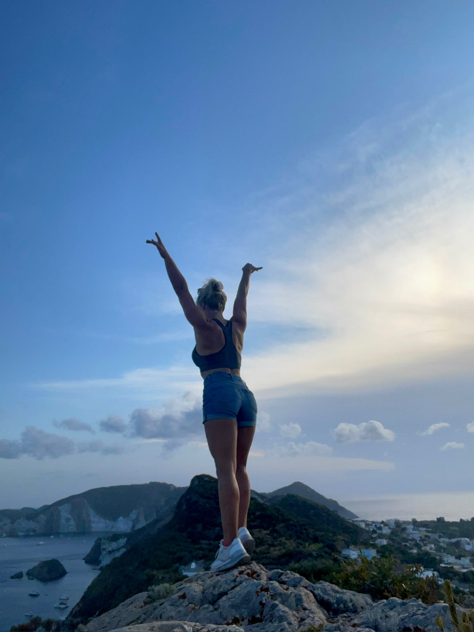 Nicole mit erhobenen Armen auf einem Berggipfel über dem Meer
